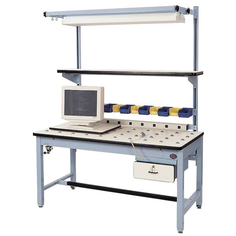 Rotating-top industrial workstation with a white perforated surface, mounted CRT monitor, multiple small parts bins in yellow and blue, overhead lighting, upper utility shelf, and integrated power strip on a light blue steel frame.